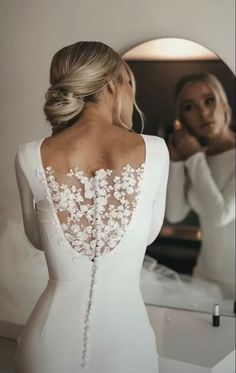 the back of a woman's wedding dress in front of a mirror with her reflection