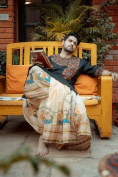 a man sitting on a yellow bench with an open book in his hand and looking at the camera