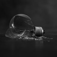 a broken light bulb laying on the floor in black and white photo with water droplets around it