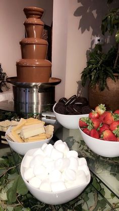 desserts are arranged on a glass table with chocolate fountain in the background