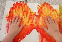 two hands are holding orange and yellow flowers on paper with newspaper pages in the background