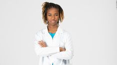 a woman with dreadlocks standing in front of a white background wearing a lab coat