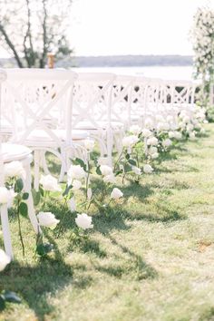 rows of white chairs lined up in the grass with flowers on each row and greenery