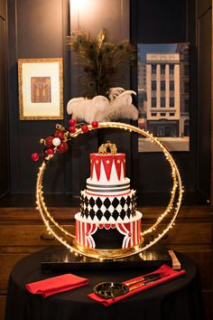 a three tiered circus cake with lights around it on a black table cloth and red napkins