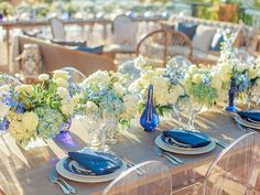 the table is set with blue and white floral centerpieces, silverware, and napkins