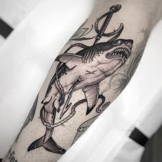 a man's arm with a shark and anchor tattoo on the left side of his arm