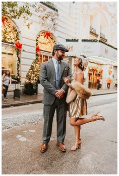 a man and woman are standing on the street in front of christmas decorations, one is wearing a fur stole