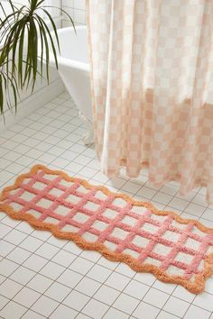 a pink and orange bathroom rug on the floor next to a bathtub with a shower curtain