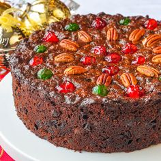 a chocolate cake topped with nuts and cherries on top of a white platter