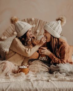 two young women sitting on a bed talking and having fun with each other while wearing winter hats