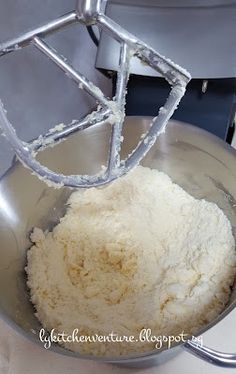 a metal bowl filled with white flour on top of a counter next to a mixer