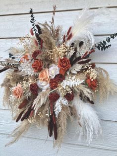 an arrangement of dried flowers and feathers on a wall