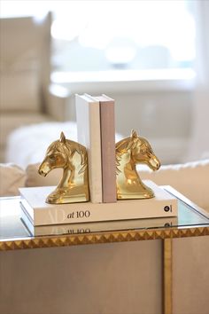 two golden horse bookends sitting on top of each other next to a coffee table