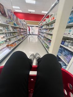 the legs of a person sitting in a shopping cart at a grocery store aisle with shelves full of products