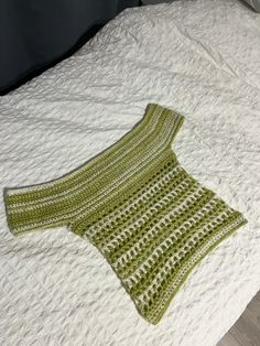 a green crocheted sweater laying on top of a white bed cover with pillows