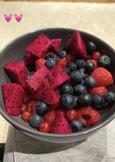 a bowl filled with berries and blueberries on top of a white table next to a pink heart