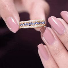 a woman's hand holding a ring with blue stones on it and gold band