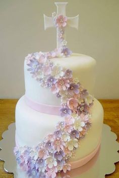 a three tiered cake decorated with flowers and a cross