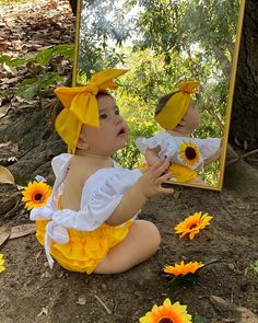 a baby sitting on the ground in front of a mirror with sunflowers around it