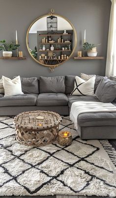 a living room with grey couches and white rugs on the floor in front of a round mirror