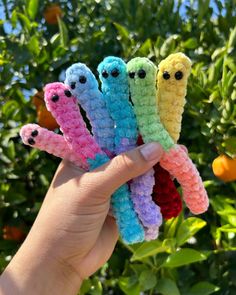 a hand holding five crocheted worms in front of some orange tree branches