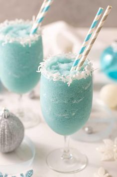 two glasses filled with blue liquid and topped with candy canes next to christmas ornaments