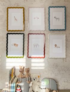 four framed pictures hang on the wall above stuffed animals and books in a child's room