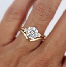 a woman's hand with a diamond ring on top of her finger and gold band