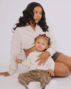 a woman sitting on the ground with a baby in her lap and holding an electronic device