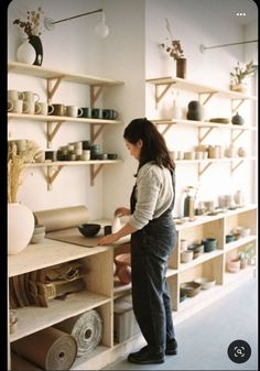 a woman standing in front of shelves filled with pottery