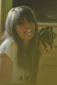 a woman taking a selfie in front of a mirror with a camera on her shoulder