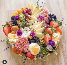 a platter filled with cheese, fruit and flowers on top of a wooden table