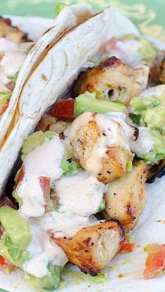 two tacos with chicken, avocado and tomato on them sitting on a green plate