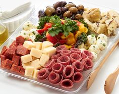 an assortment of meats and cheeses in a plastic container with olives on the side