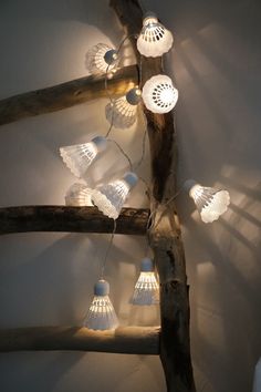 some lights that are hanging from a tree branch in a room with white walls and wood beams