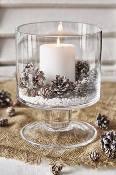 a candle in a glass bowl filled with snow and pine cones