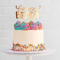 a birthday cake with sprinkles and a gold happy birthday sign on top