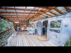 an airstream sits on a wooden deck with chairs and table in the foreground