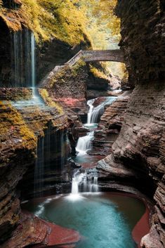 a small waterfall in the middle of a canyon with a bridge over it and water running through