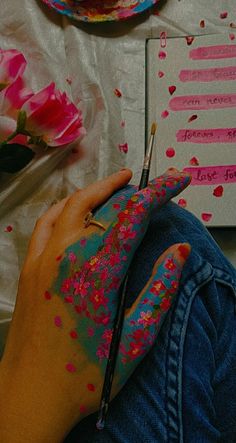 a person is painting on their left hand with pink and blue flowers in the background