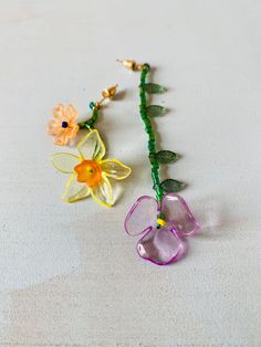 two flowers are attached to a green beaded necklace on a white surface, one is yellow and the other is pink