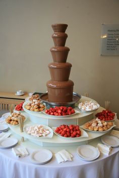 a chocolate fountain is set up on a table with plates and desserts around it