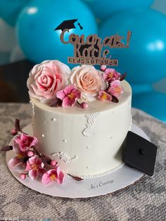 a white cake with pink flowers and a graduation cap on top is sitting on a table