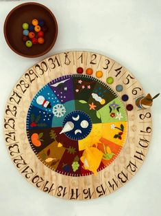 a wooden plate with letters and numbers on it next to a bowl filled with beads