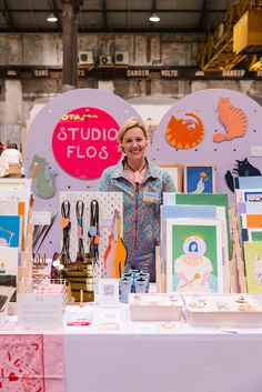 a woman standing in front of a table with art on it and other items for sale