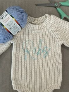 a baby sweater with the word hello kitty written on it next to yarn and scissors