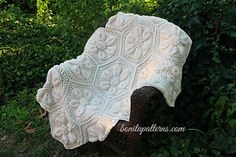 a white crocheted blanket sitting on top of a wooden chair in the grass