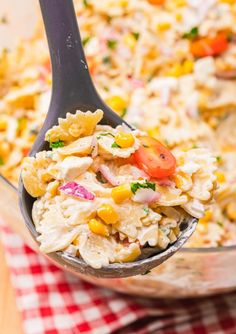 a spoon full of macaroni salad with tomatoes and corn