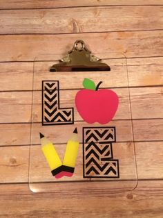 a clipboard with an apple, pencils and tape on it sitting on top of a wooden table