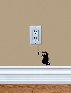 a black cat sitting on top of a wooden floor next to an electrical outlet wall